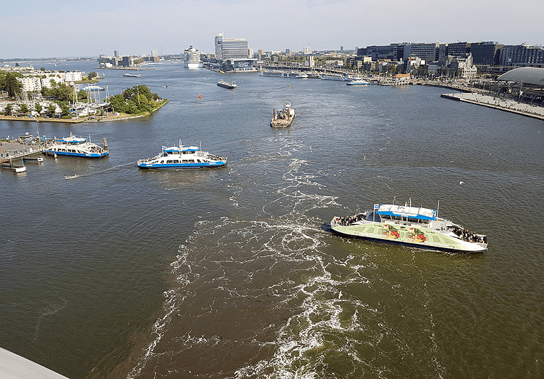 Vanaf het achterdek van een 18 of 19 dekken hoog cruiseschip zoals de MSC Euribia, heb je een prachtig uitzicht over Amsterdam en het gekrioel van ponten, vrachtschepen en kleine bootjes op het IJ. © Nico van Dijk / Decruisegids.nl